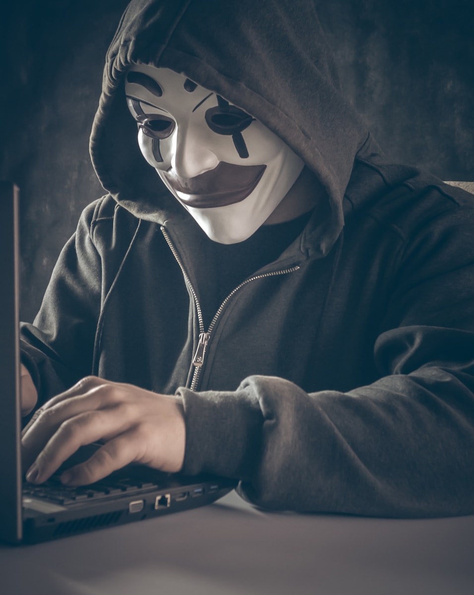 a person wearing a mask using a laptop launching a cyberattack