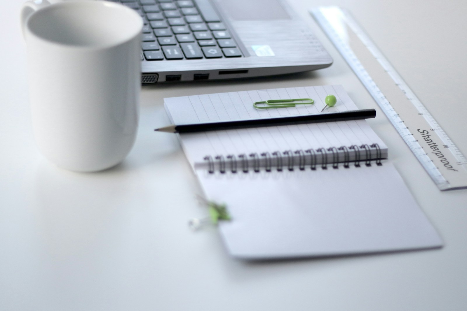 black pencil on ruled notepad beside white ceramic mug and gray laptop computer symbolizing small business insurance